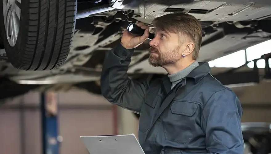 Garagiste debout inspectant le dessous dune voiture dans un garage